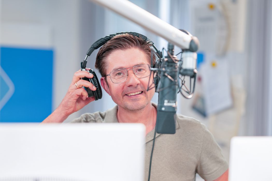 Philipp Eger mit Kopfhörern und Brille am Mikrofon im Radiostudio